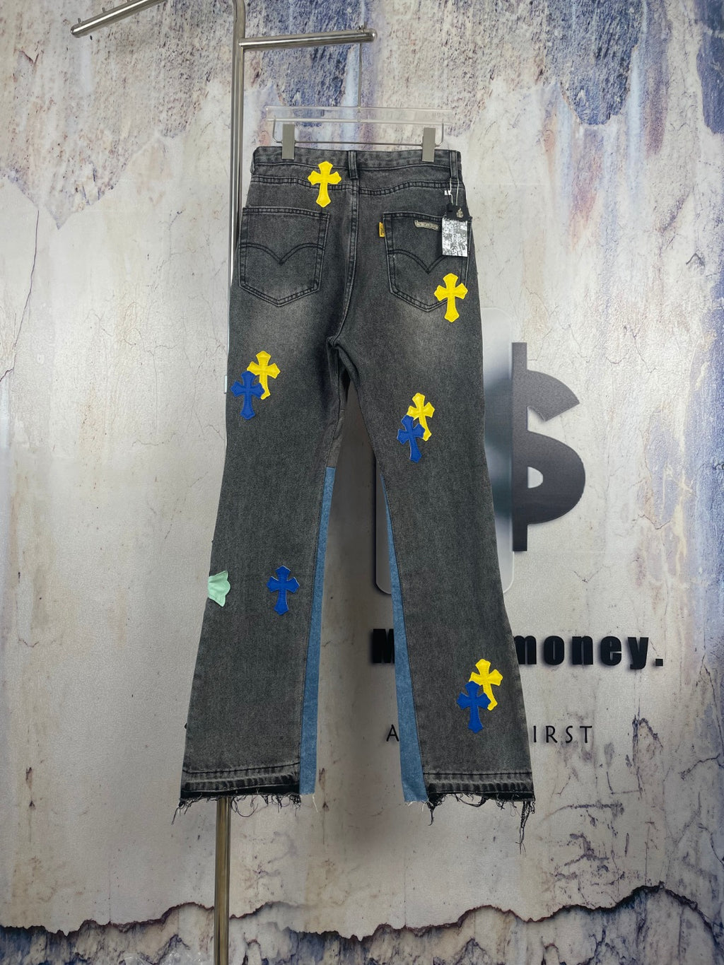 Dark denim pants with colorful cross patches and distressed, frayed hem