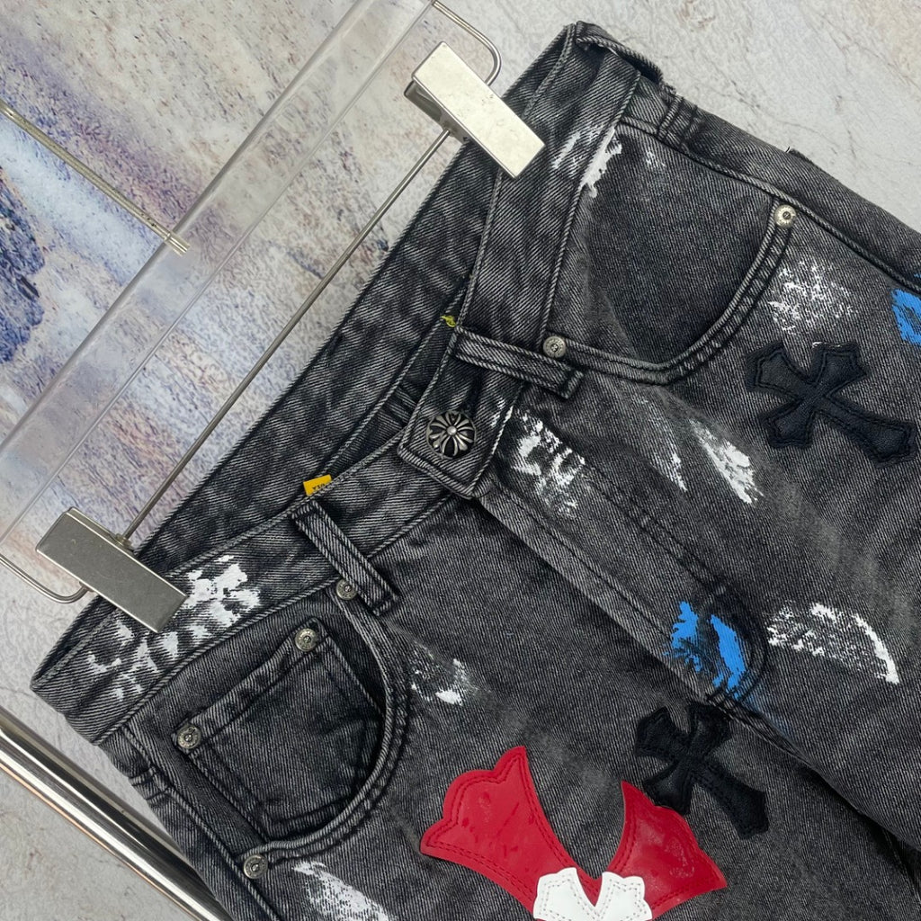 Dark denim pants close-up with distressing and colorful cross appliques