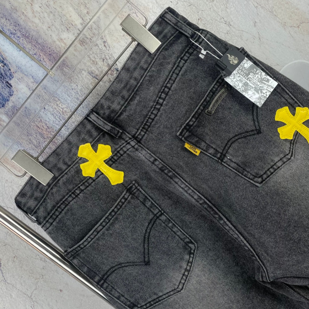 Dark denim pants with yellow cross patches, stitched pockets, and waistband