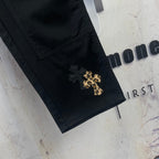 Black pants with V-shaped pocket stitching and gold cross patch on the leg