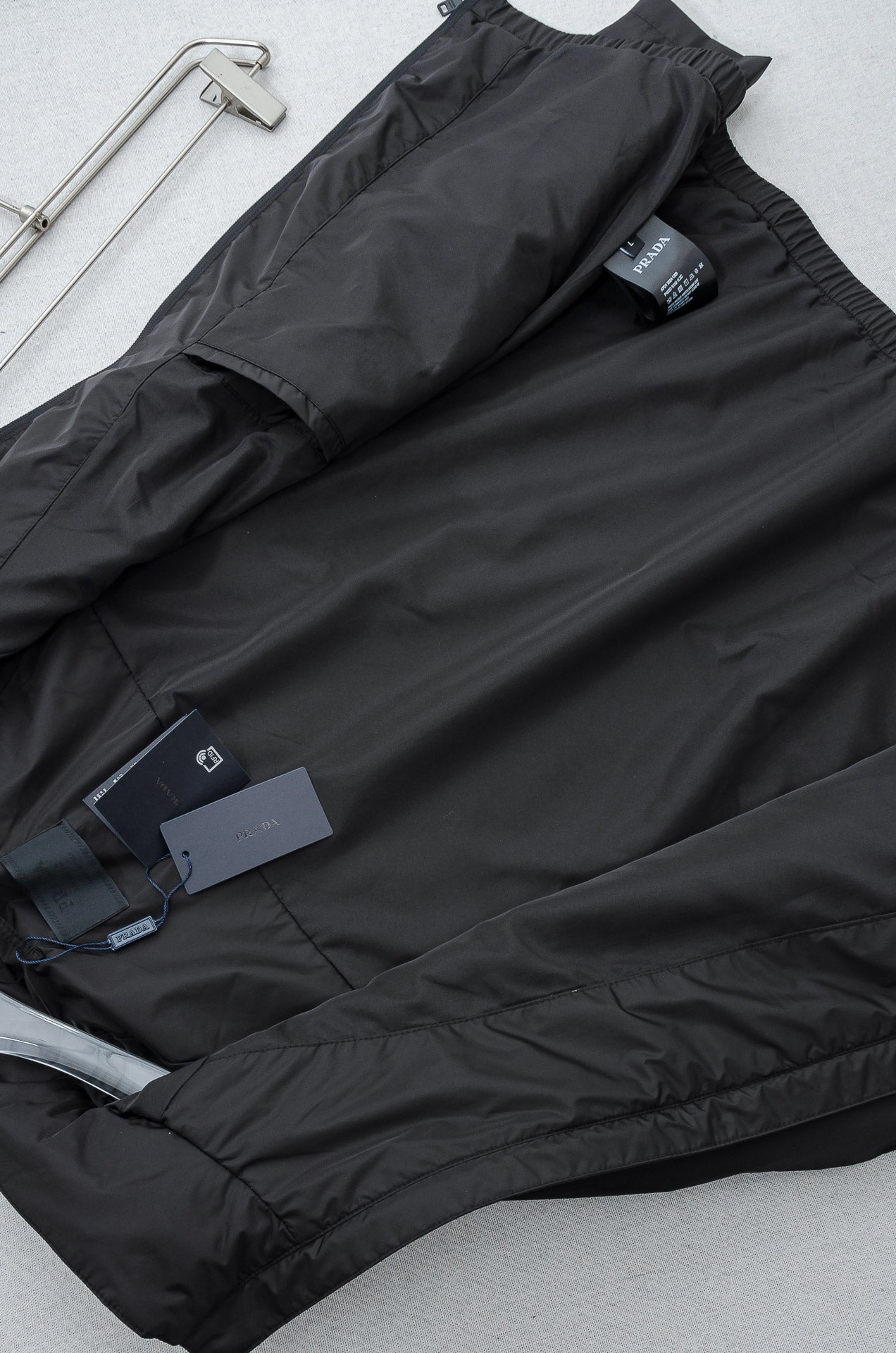 Prada long jacket laid flat with dark outer fabric and attached product tags