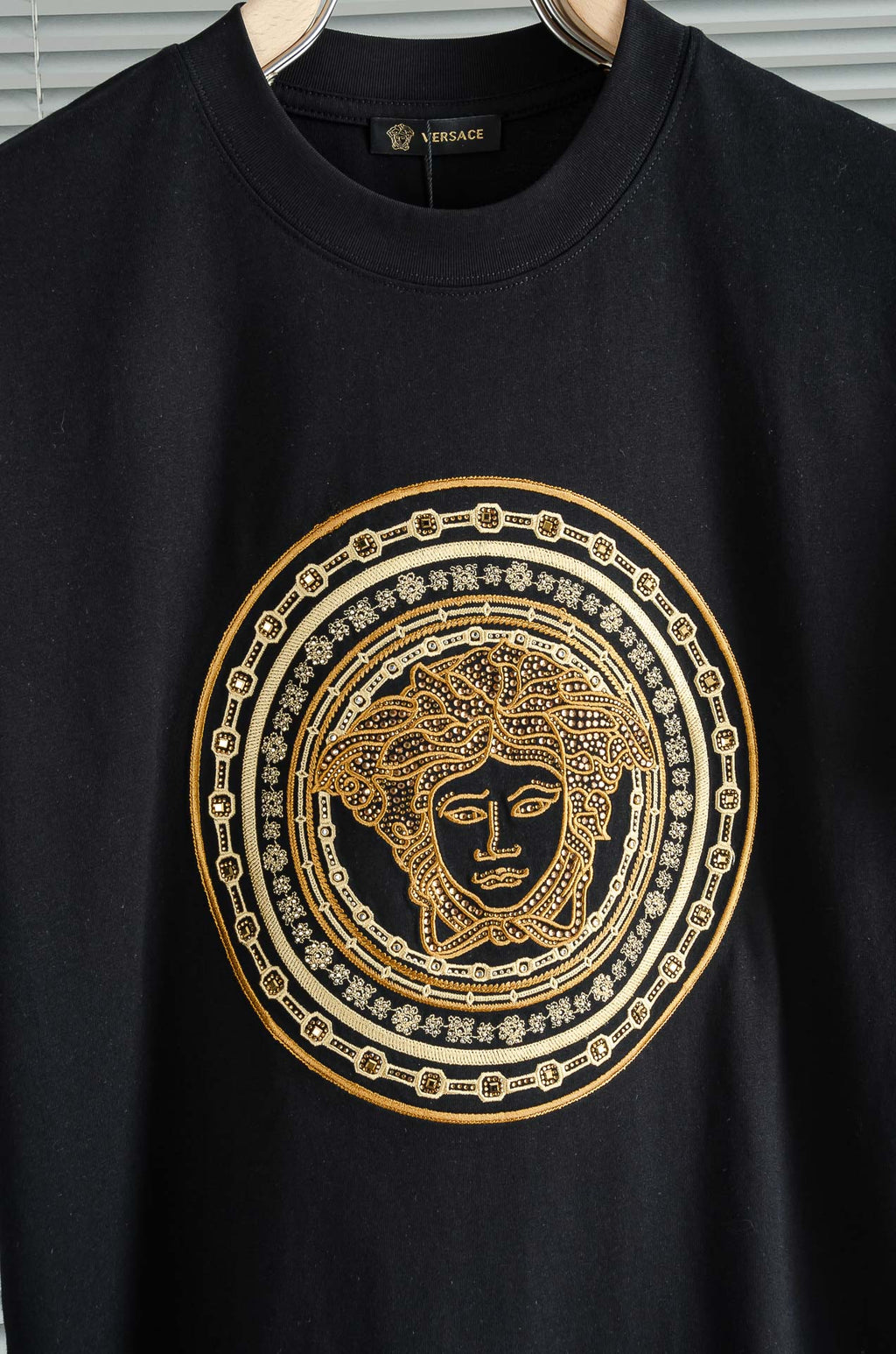 Black T-shirt close-up of gold Medusa-style emblem