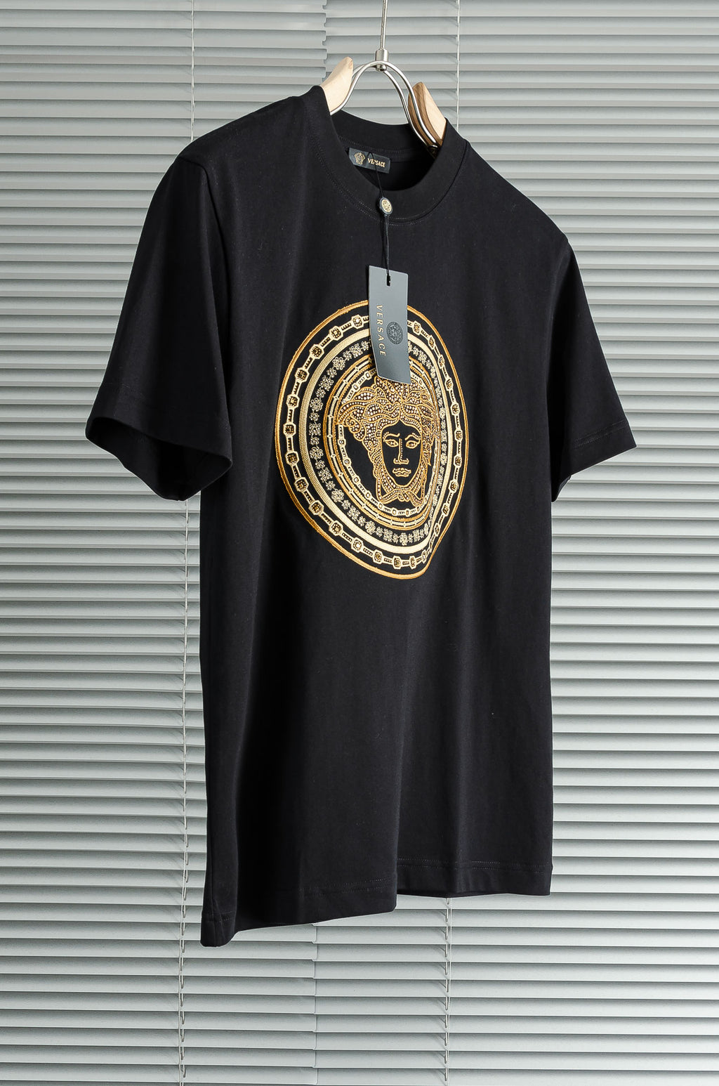 Black T-shirt with gold medallion graphic and hanging tag on the neckline
