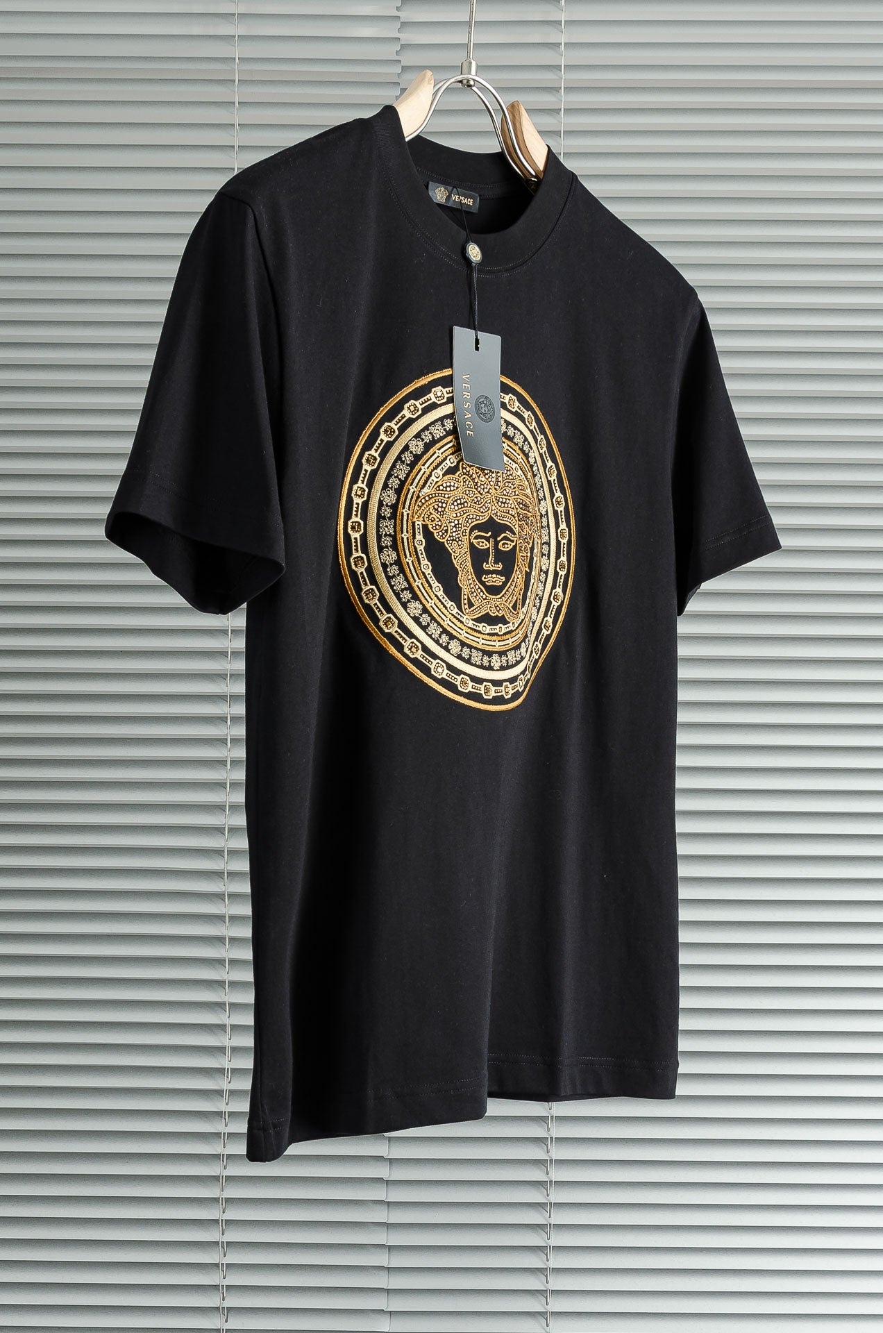 Black T-shirt with gold medallion graphic and hanging tag on the neckline