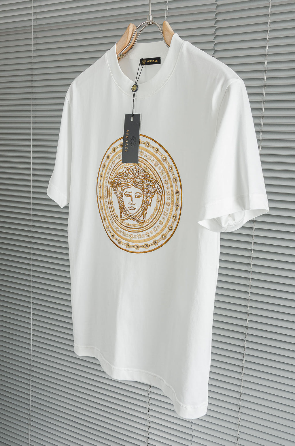 Versace white T-shirt on hanger with gold Medusa-style circular chest graphic