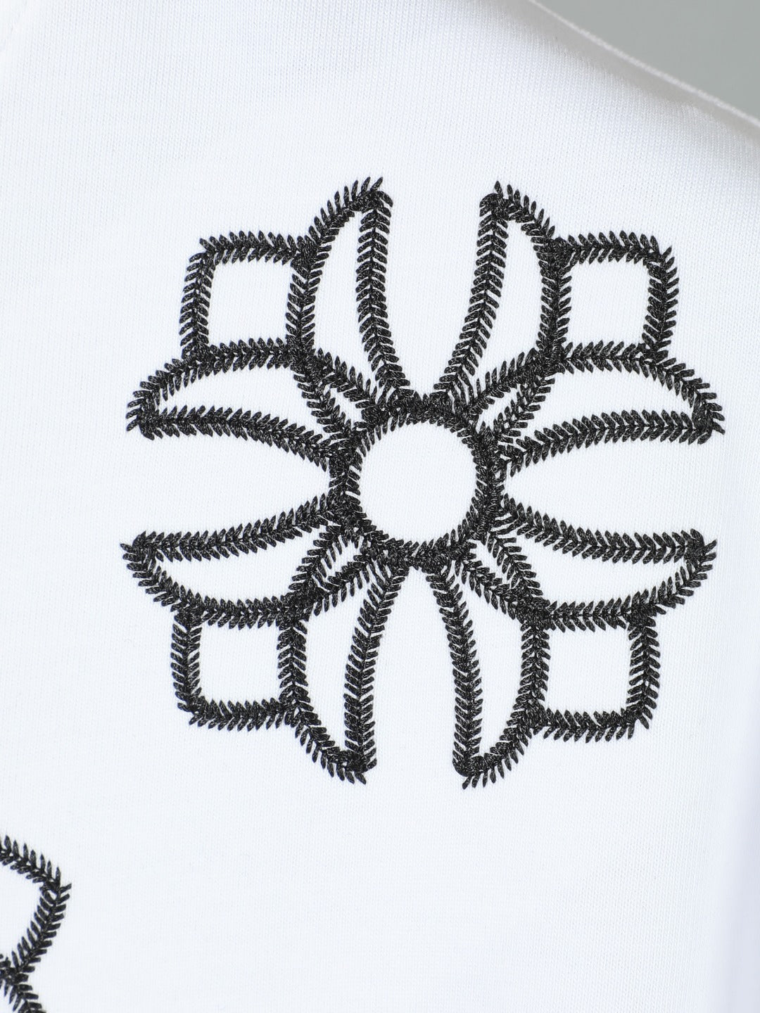 White T-shirt close-up of black embroidered flower appliqué graphic