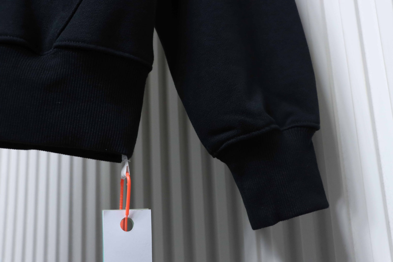 Off White hoodie sleeve cuff detail in dark fabric, hanging tag visible