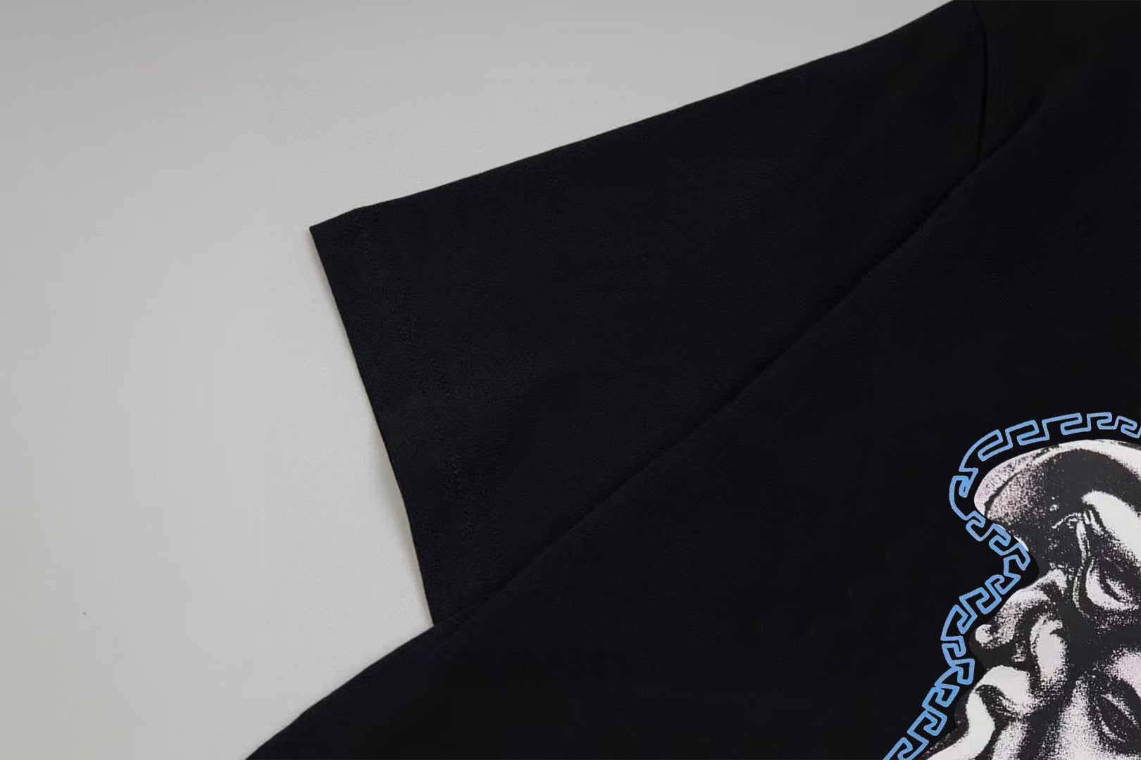 Black T-shirt sleeve with partial blue Medusa graphic