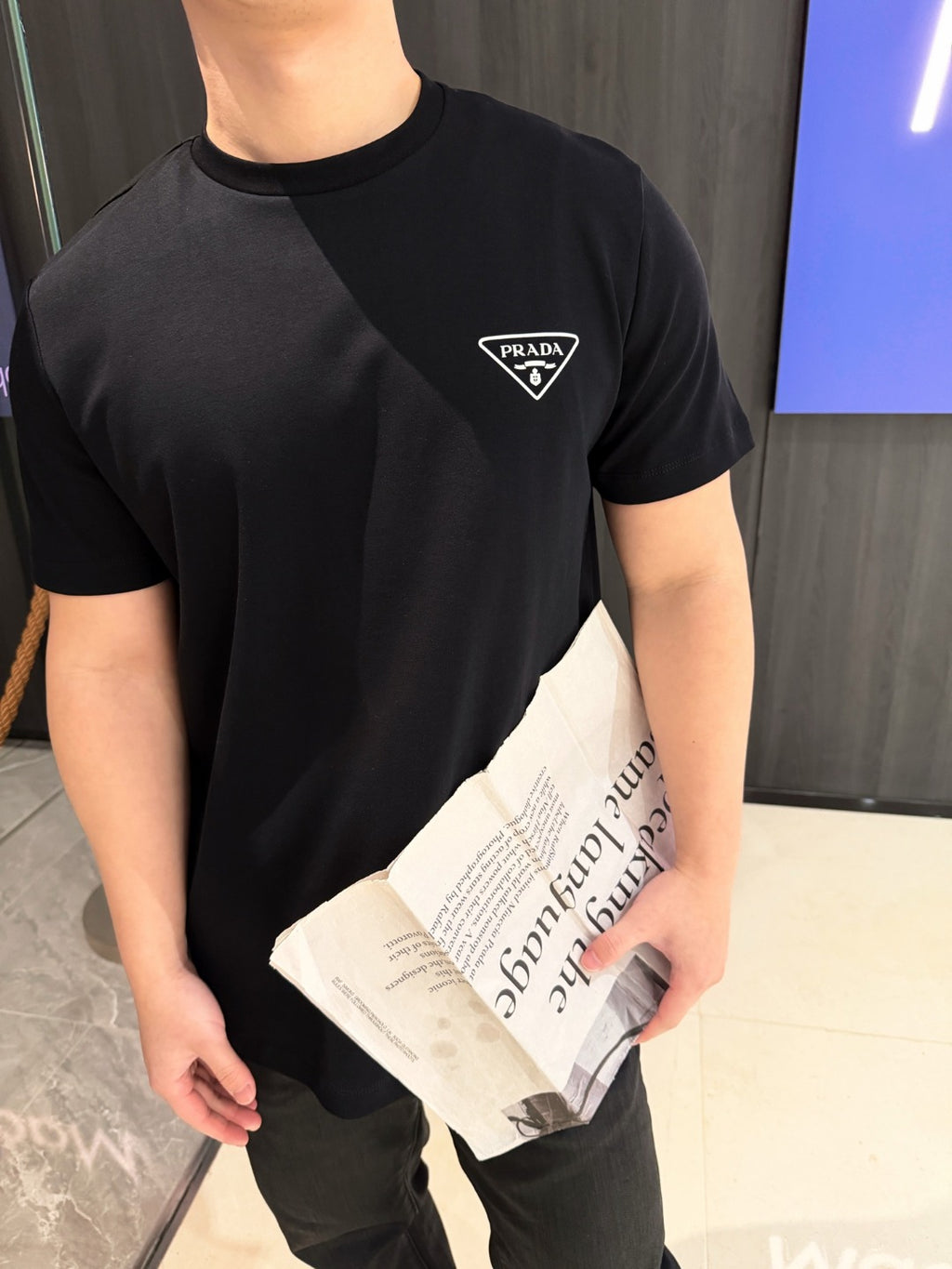 Close-up: black crew-neck T-shirt with PRADA triangular logo patch on chest