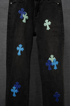 Black denim pants with scattered blue and green cross patches, side view