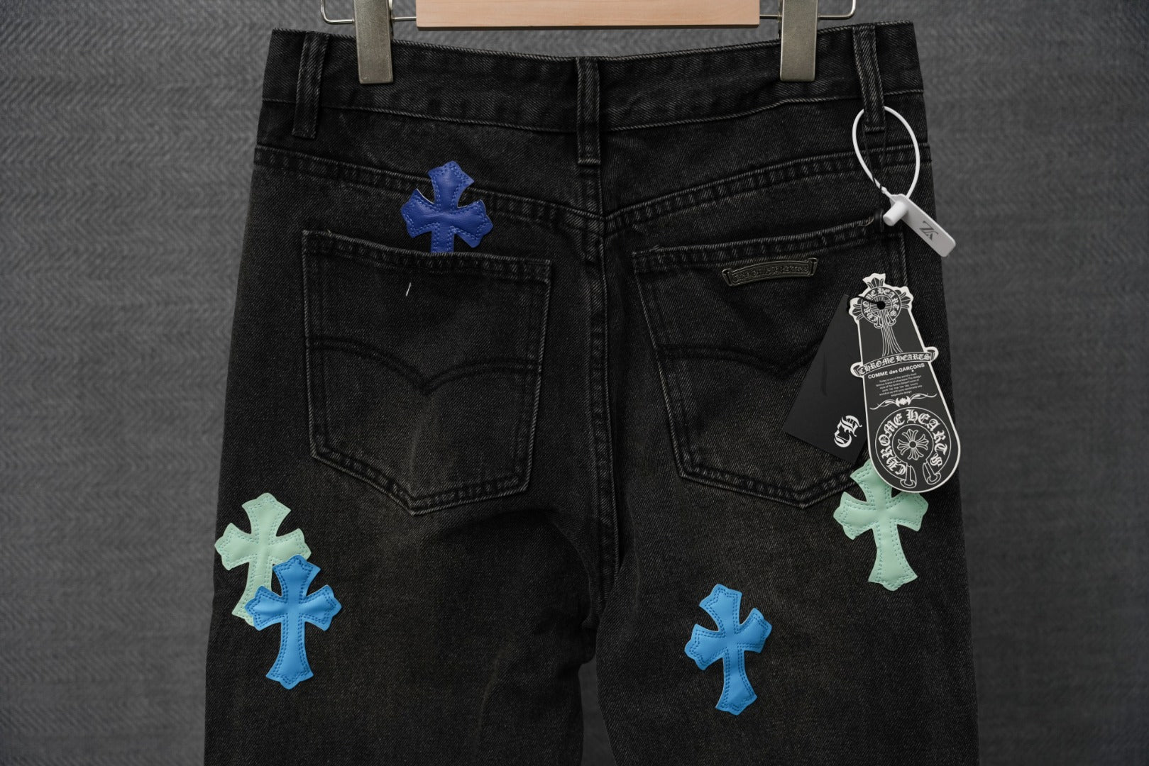 Black denim pants front view with multiple blue and green cross patches