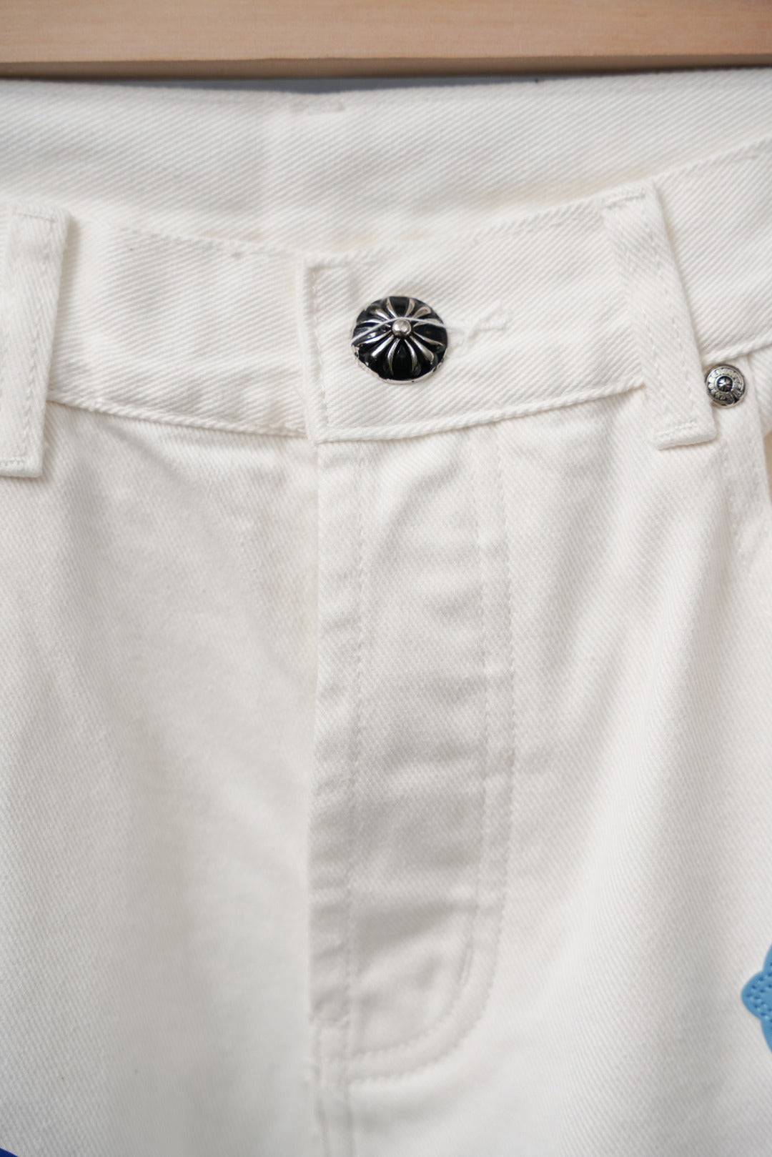 White denim pants waistband with black circular button and stitched detailing