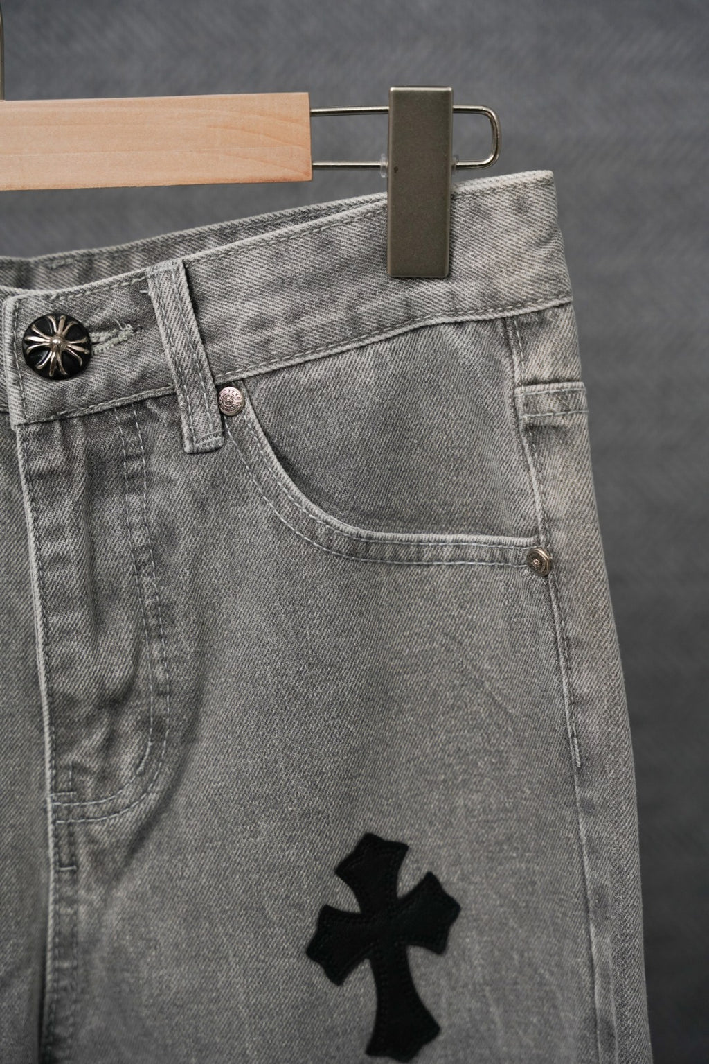 Waistband and front of gray denim pants with black cross patch