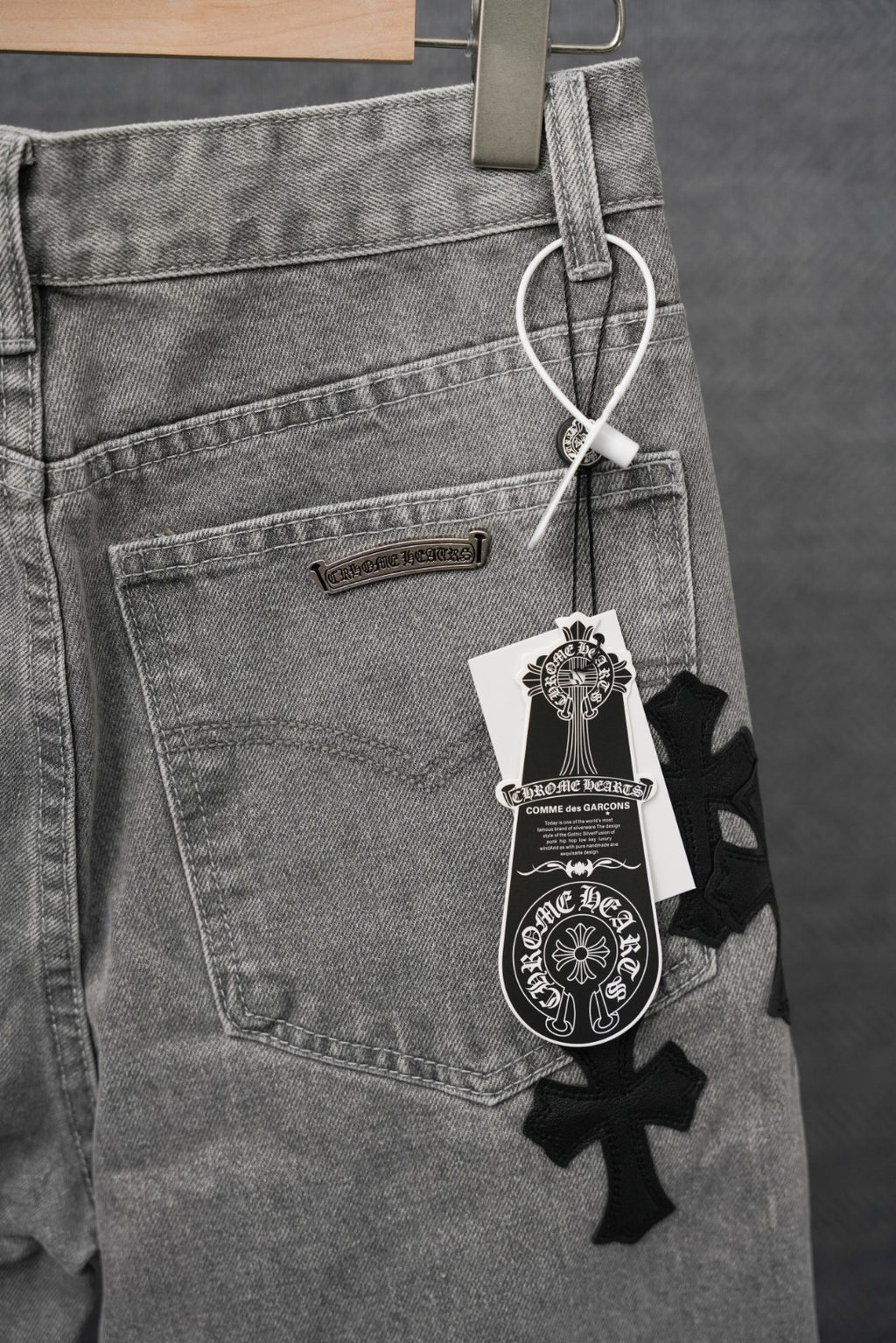Gray denim pants with label tag and black cross patch near pocket
