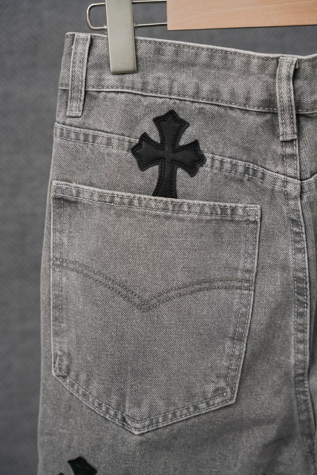Gray denim pants back pocket with black cross patch near hip