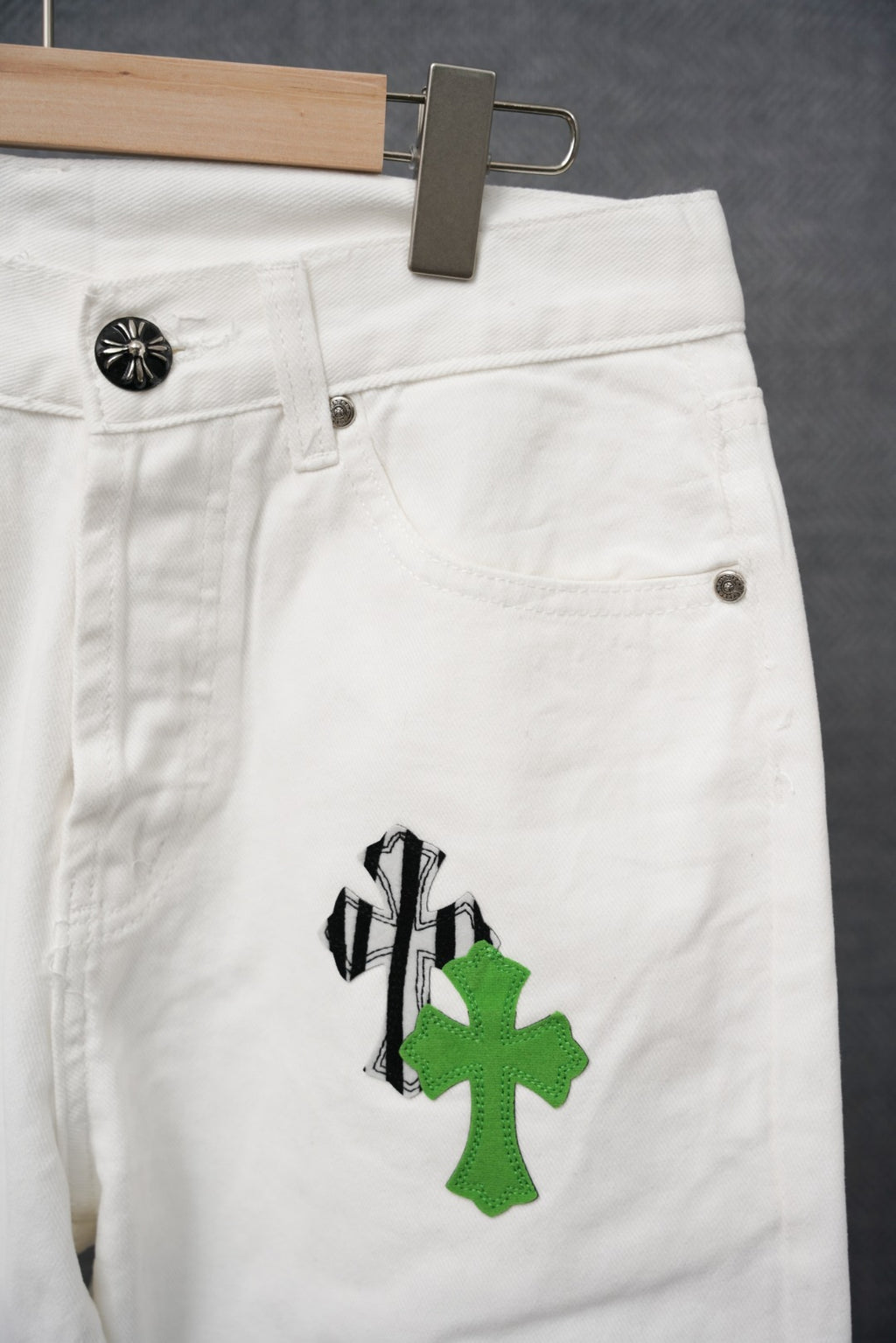 White denim pants with front button closure and pockets; green cross-like graphic patch
