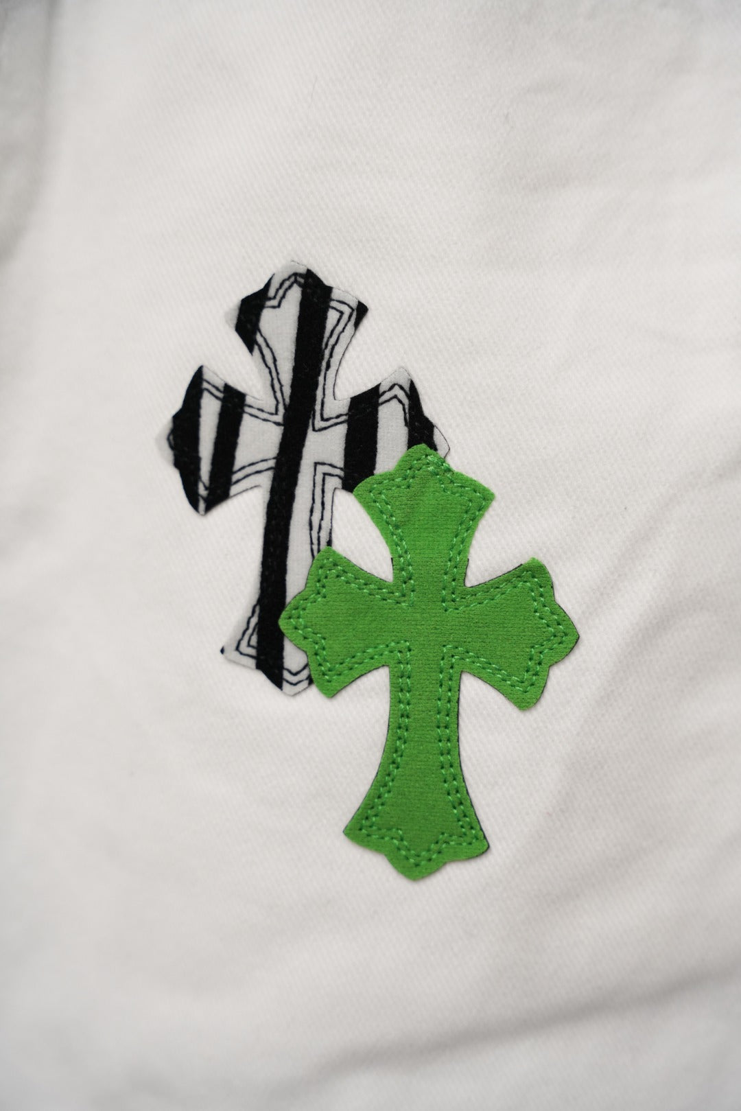 White fabric with close-up green cross-like graphic patch and black outline