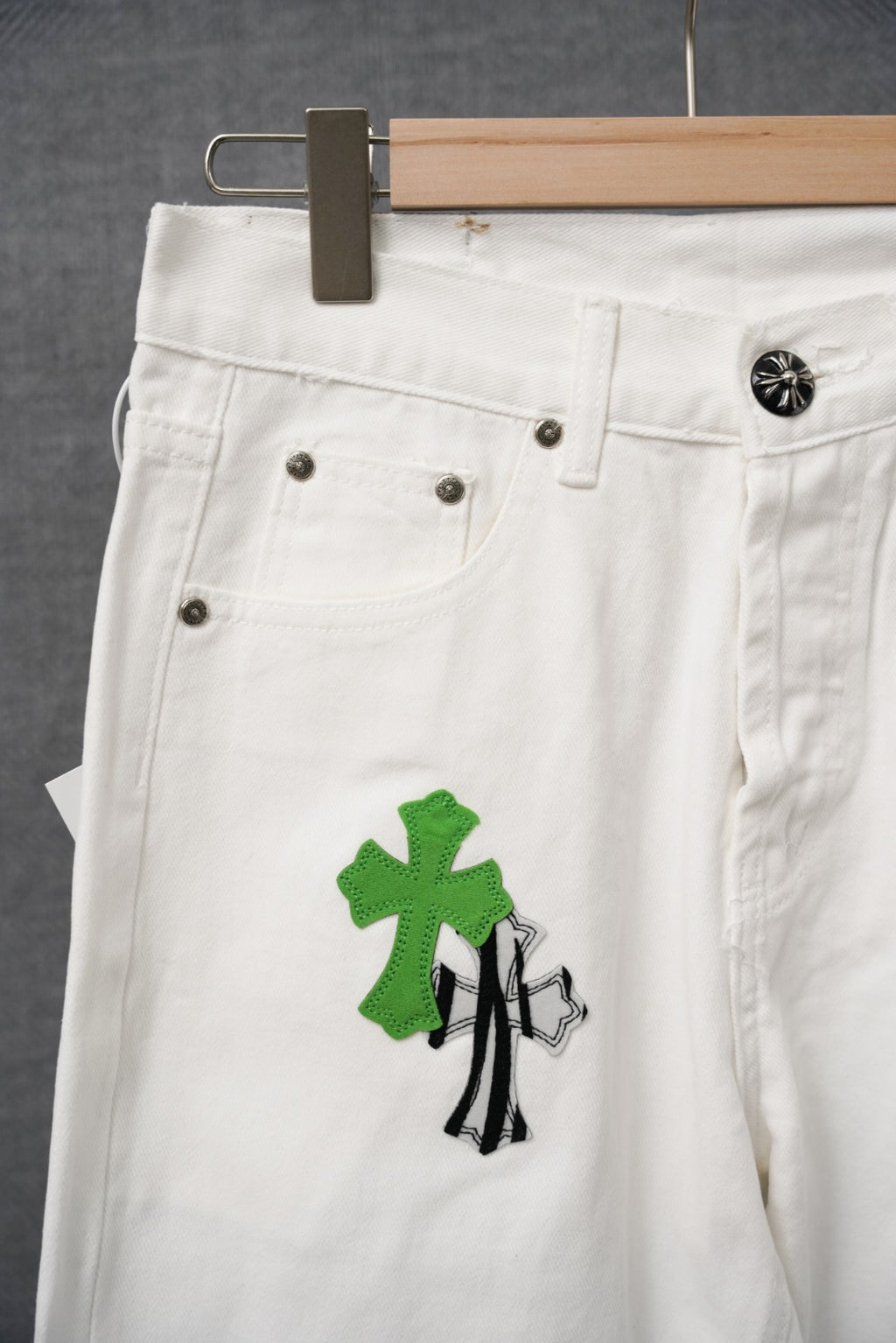 White denim pants with green cross-like graphic patch; belt loops and button detail