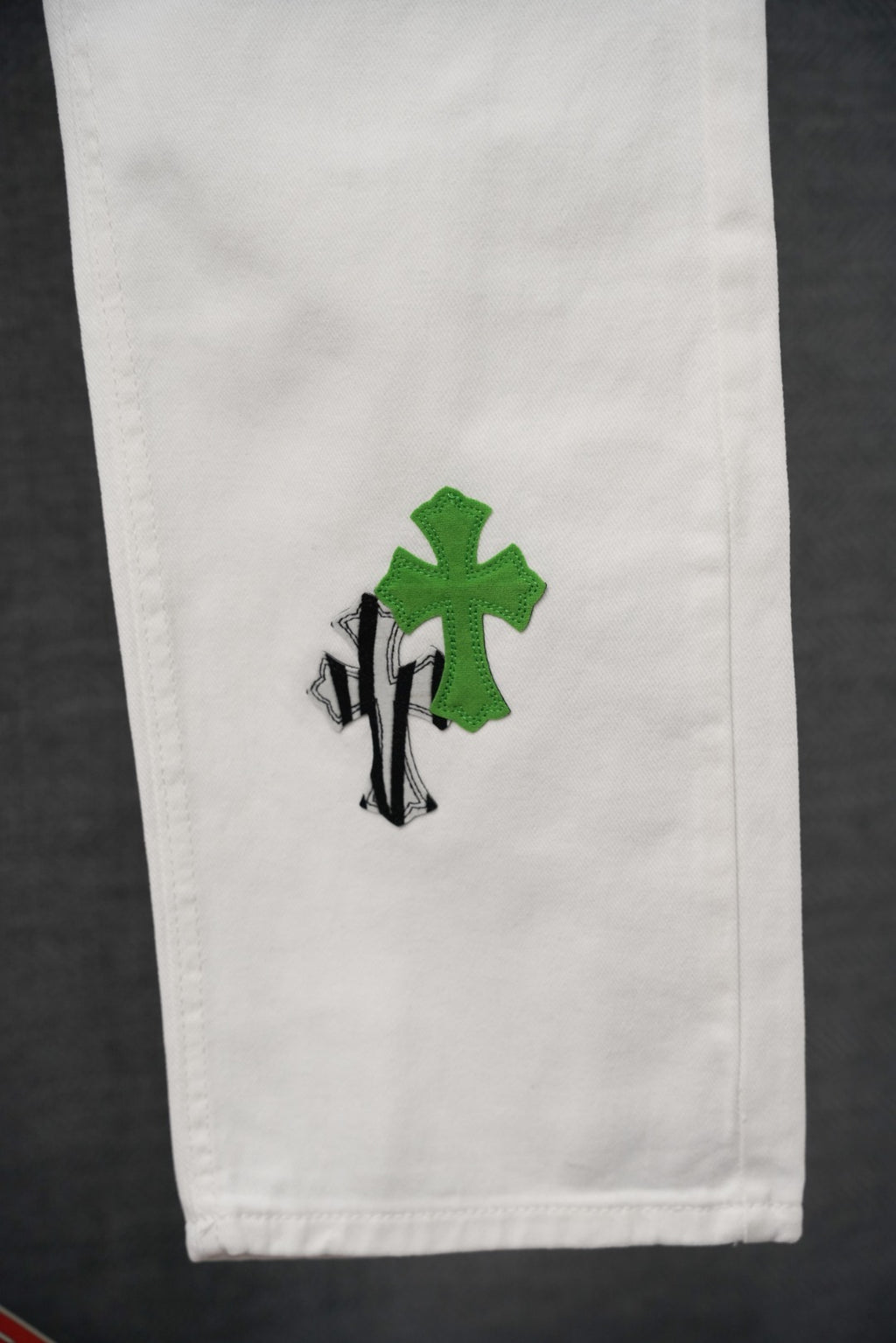 White denim leg with small green cross and black striped graphic