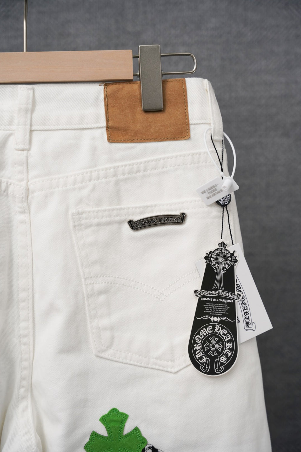 White pants on hanger with stitched pocket, black zipper, green cross patch and tag