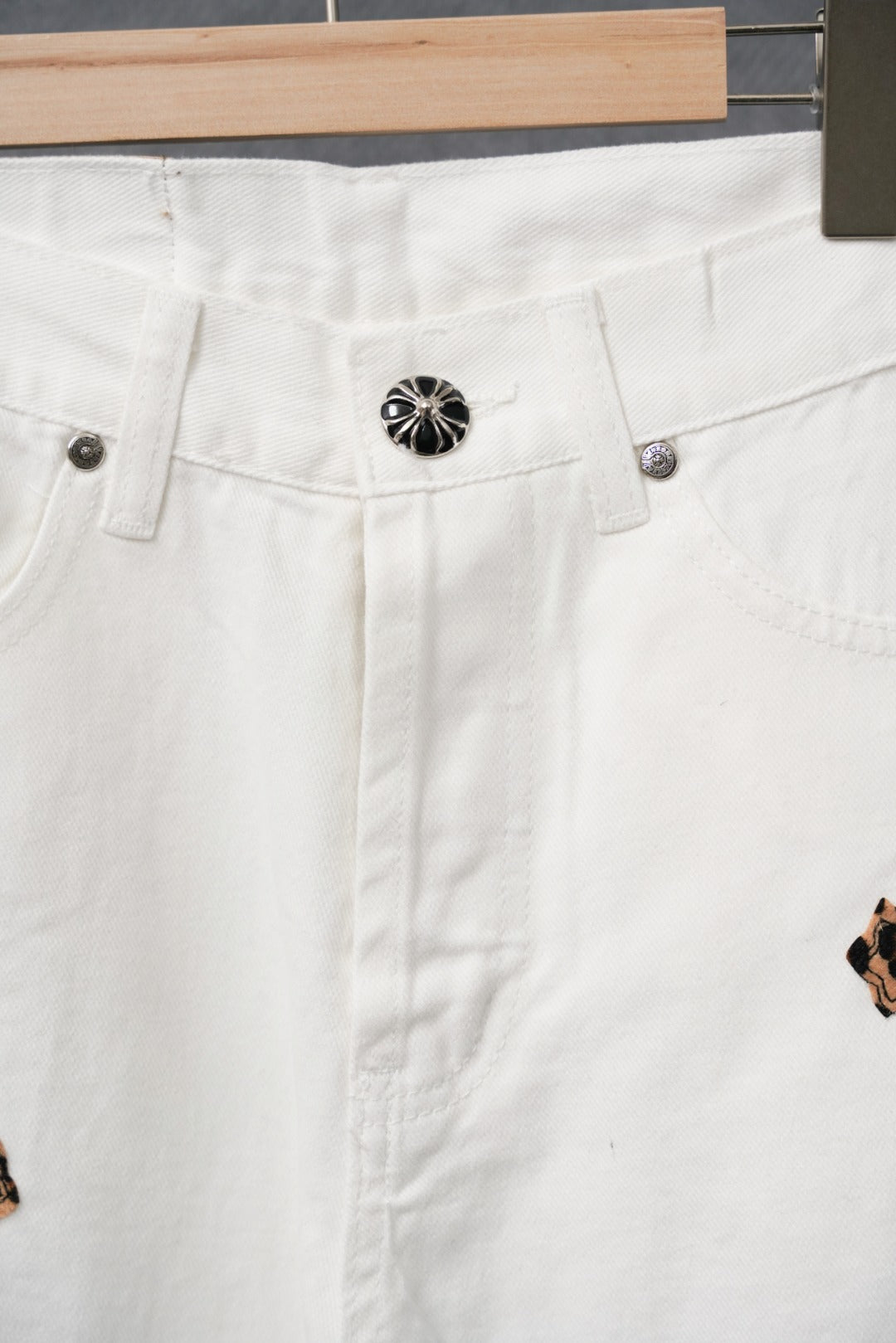 White pants close-up showing waistband buttons and a small leopard-print cross patch