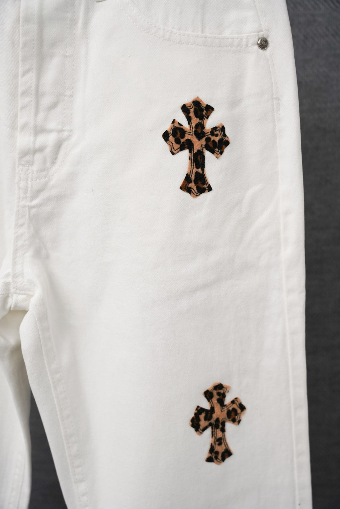 White pants close-up with leopard-print cross patch and side button detail