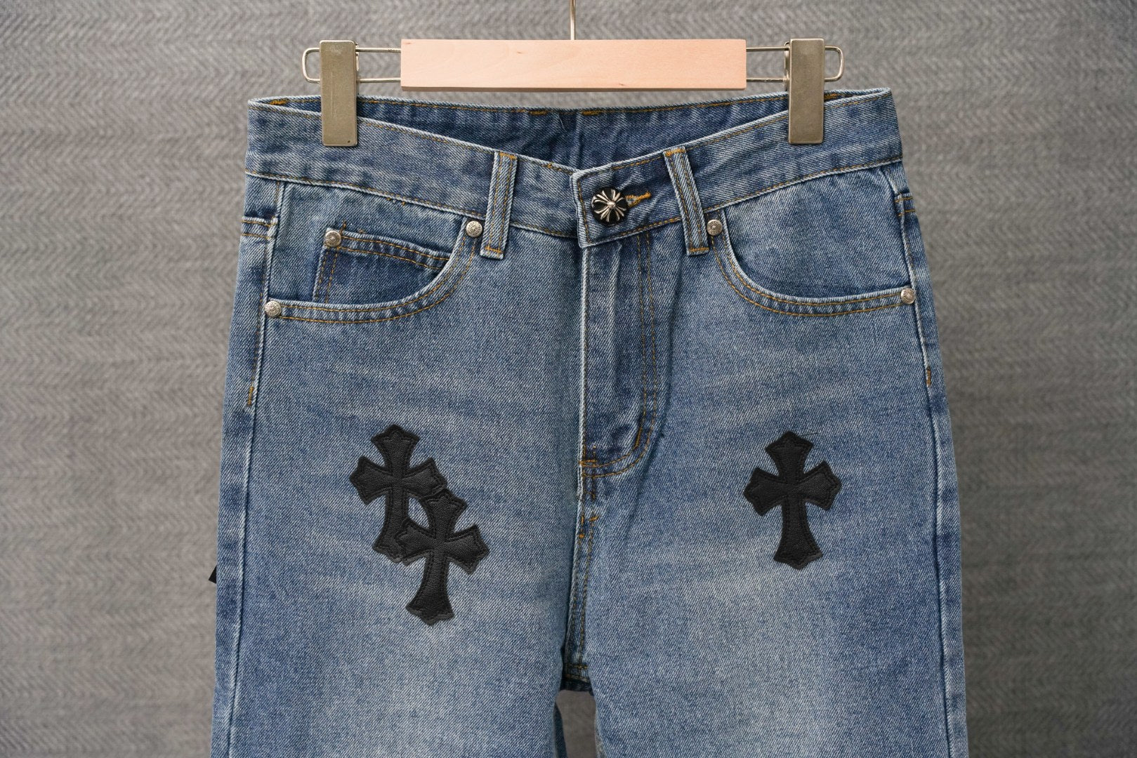 Light blue denim pants with black cross patches; front view with button fly