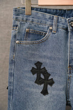 Light blue denim pants with black cross applique centered on front