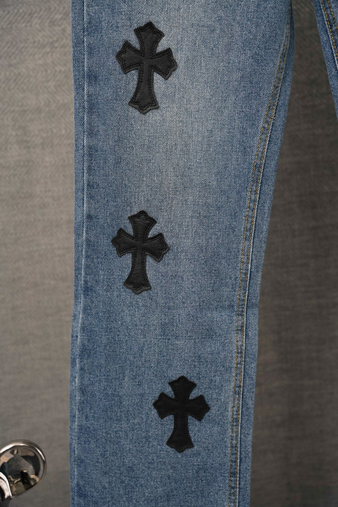Light blue denim pants side view with black cross patches spaced on leg
