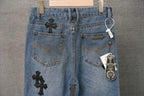 Light blue denim pants with black cross patches and front button fly, hanging tag