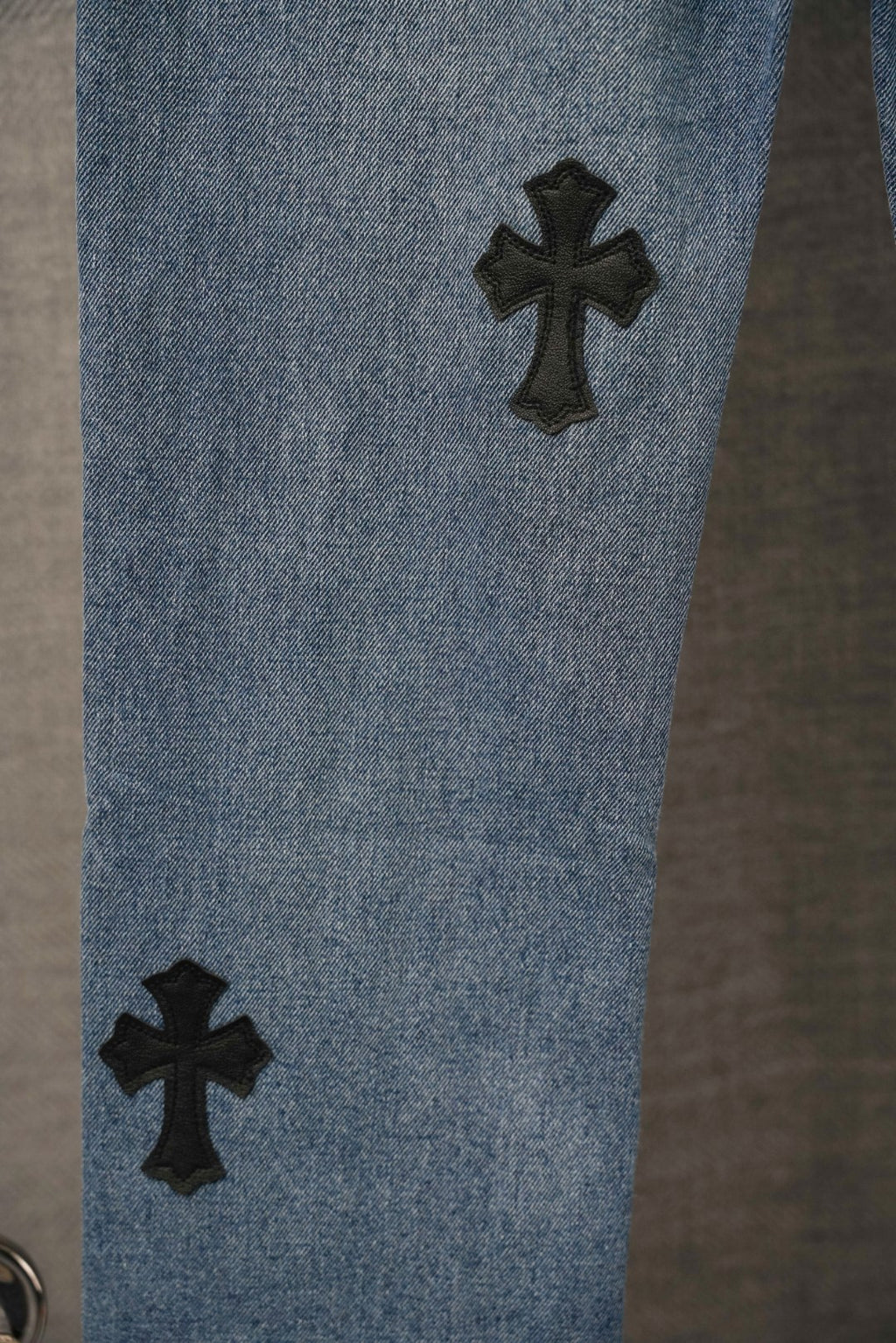 Blue denim Chrome pants leg with two black cross patches near the knee.