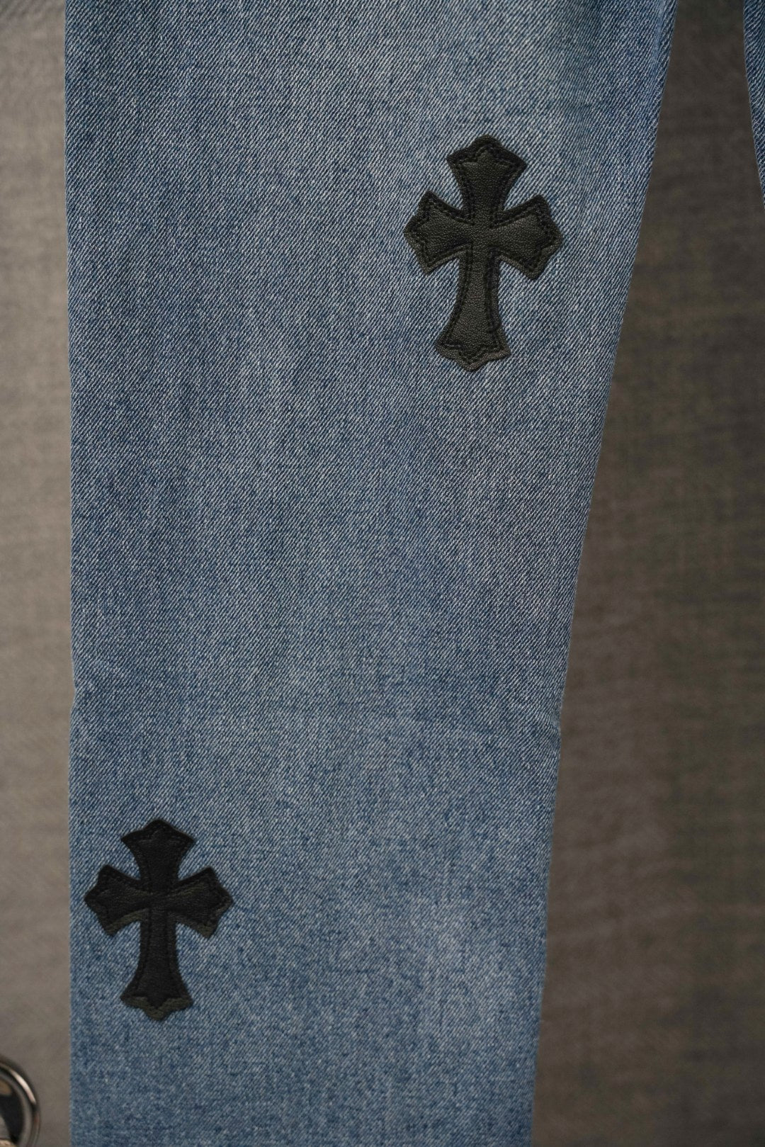 Light blue denim pants close-up with black cross patch on leg