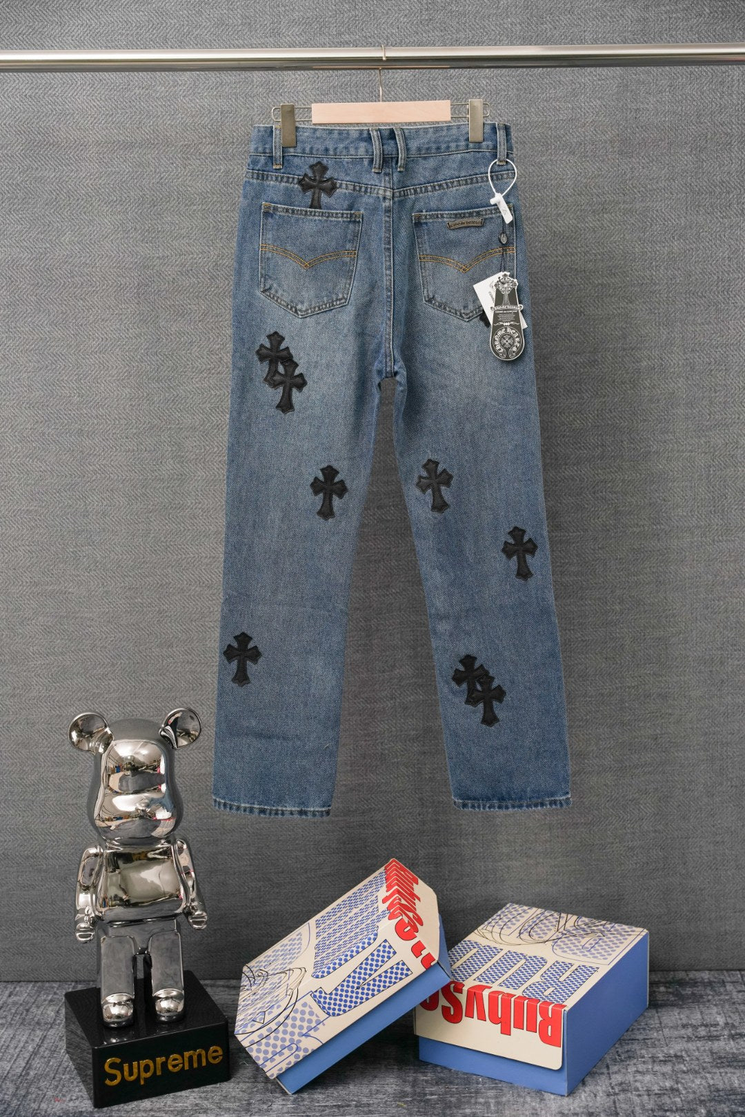 Blue denim Chrome pants with black cross patches, back view, belt loops and tag.