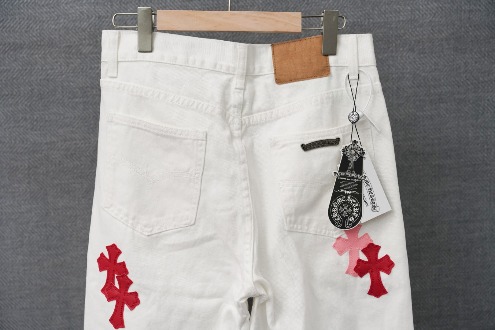 White pants with red cross applique, belt loops, and hanging brand tag