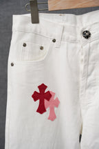 White denim pants with red cross graphic on front leg and pocket buttons