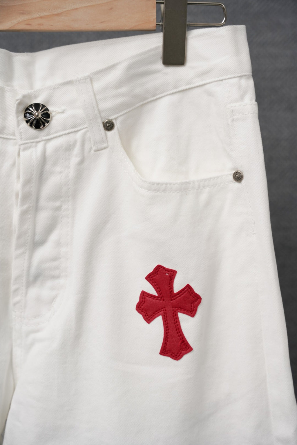 White pants with red cross applique near pocket and belt loop hardware