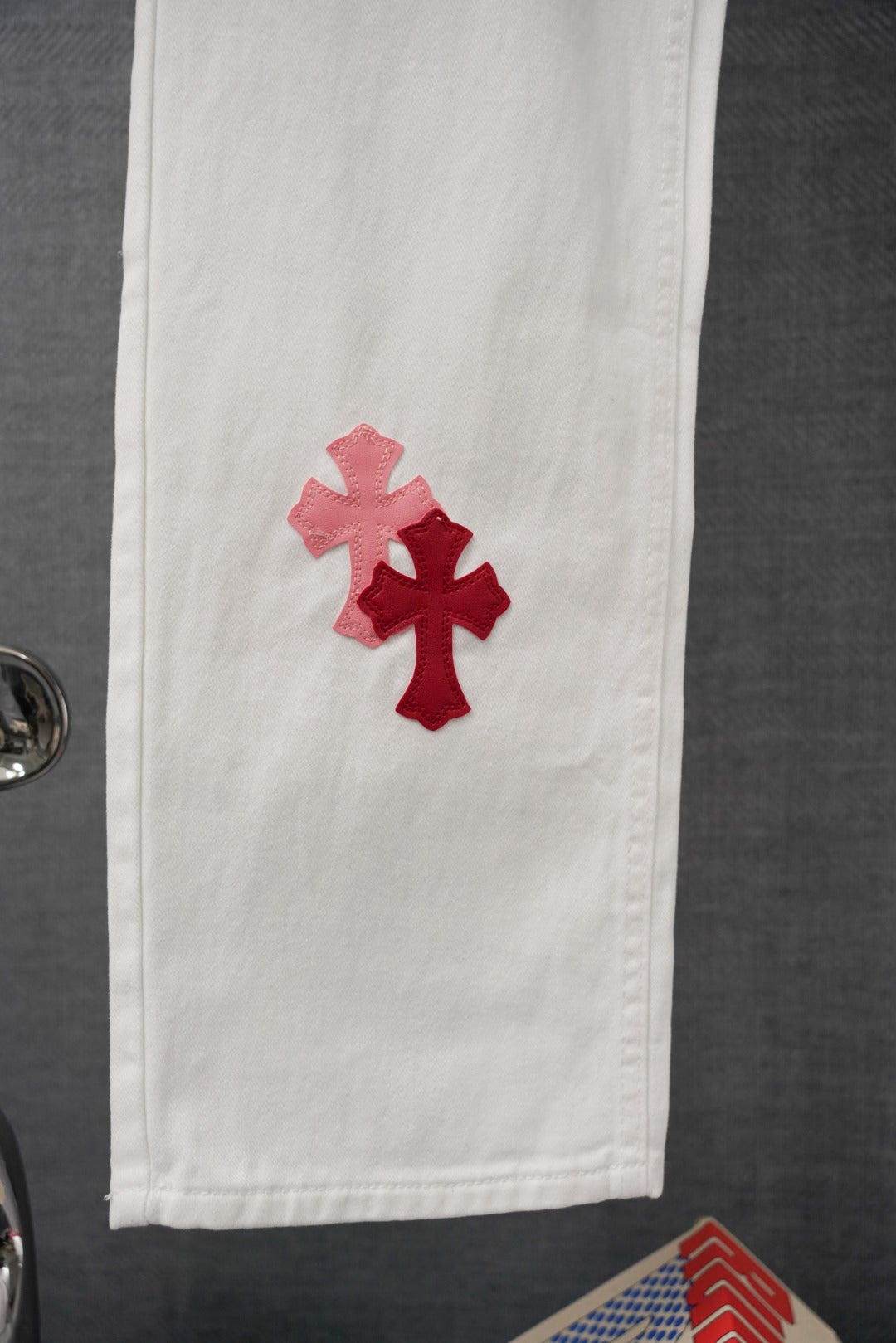White denim pants with red and pink cross patches on the lower leg