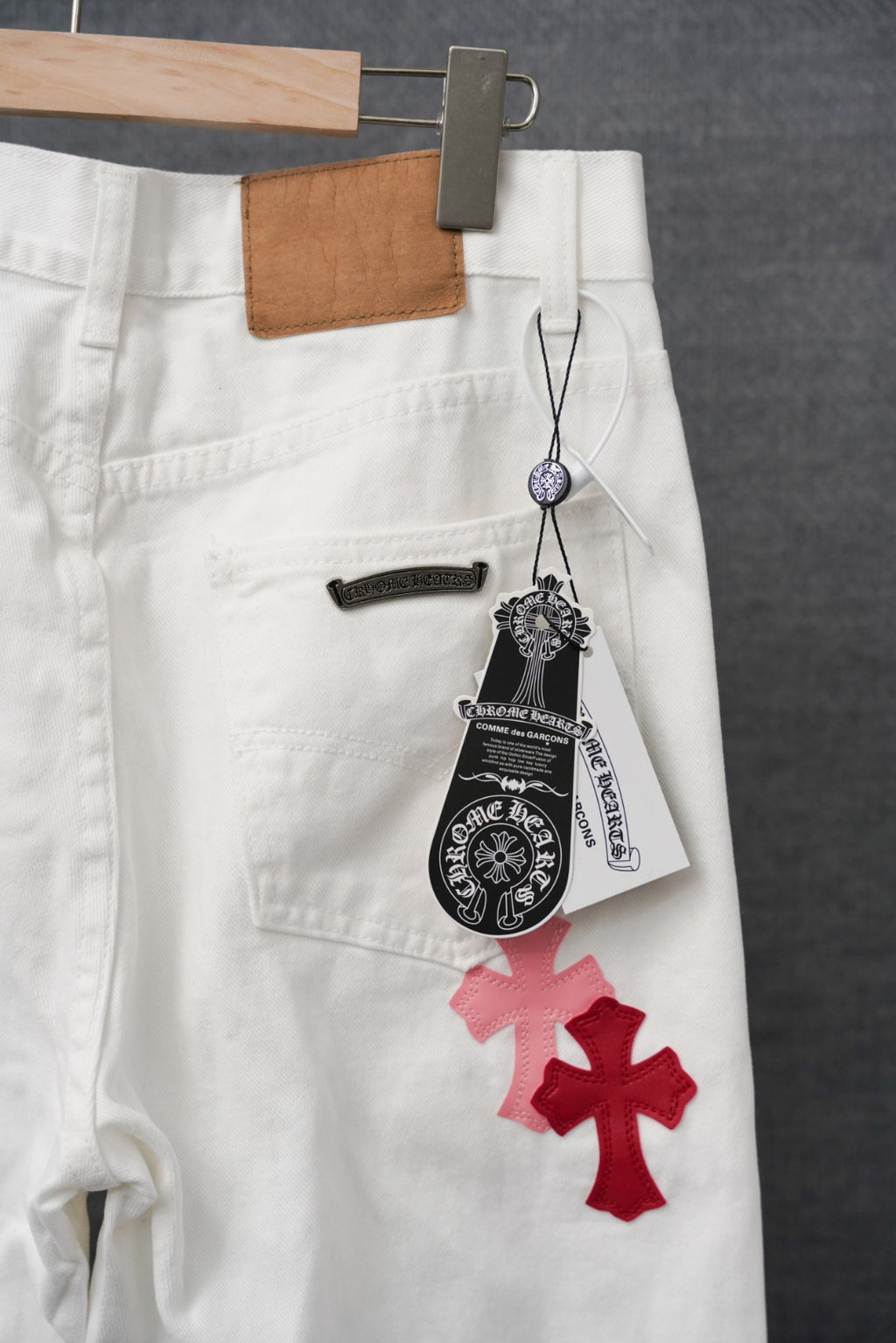 White pants with red cross applique, belt loops, and black hanging tag