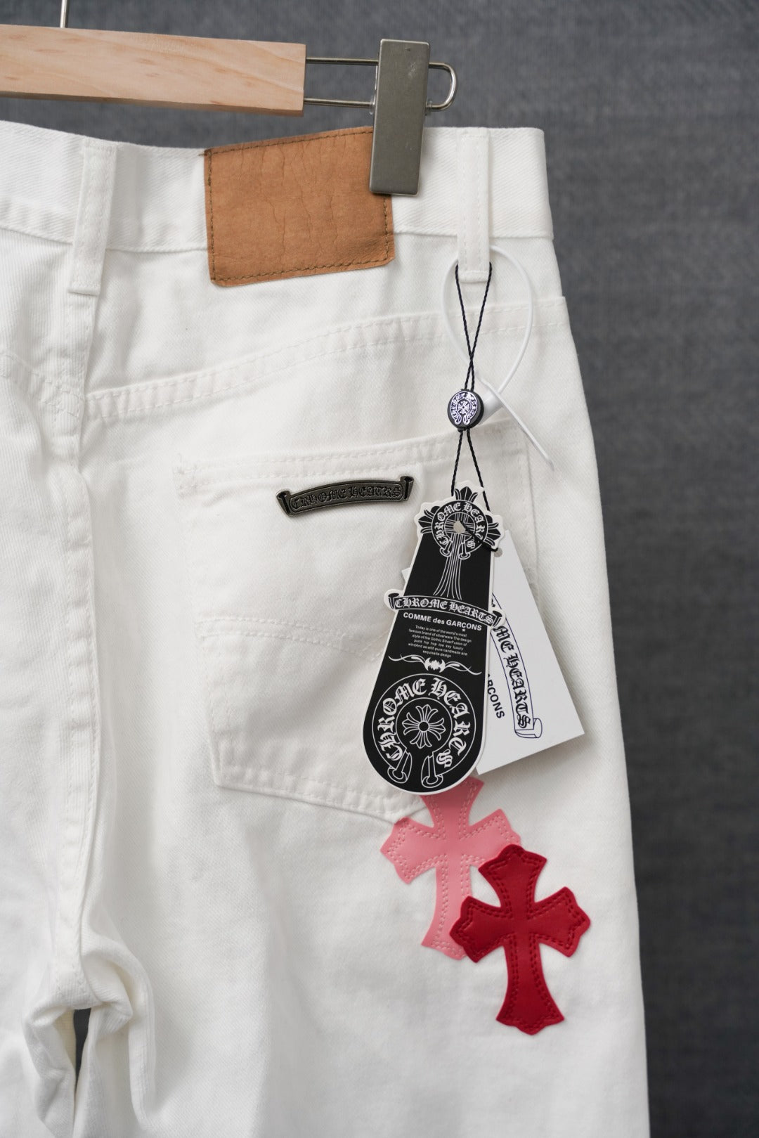 White pants with red cross applique, belt loops, and black hanging tag