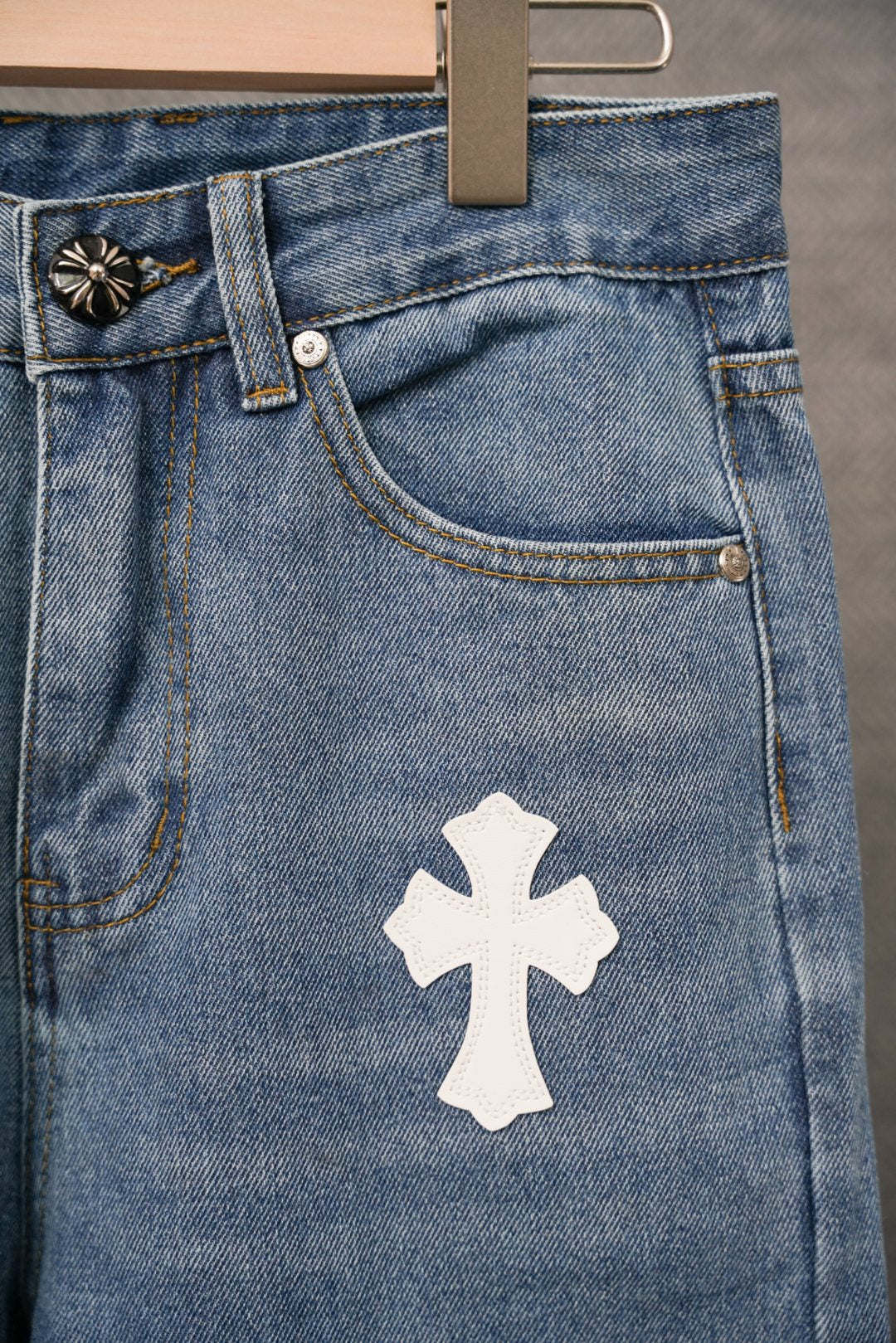Blue denim pants front pocket area with ornate button, white cross patch.