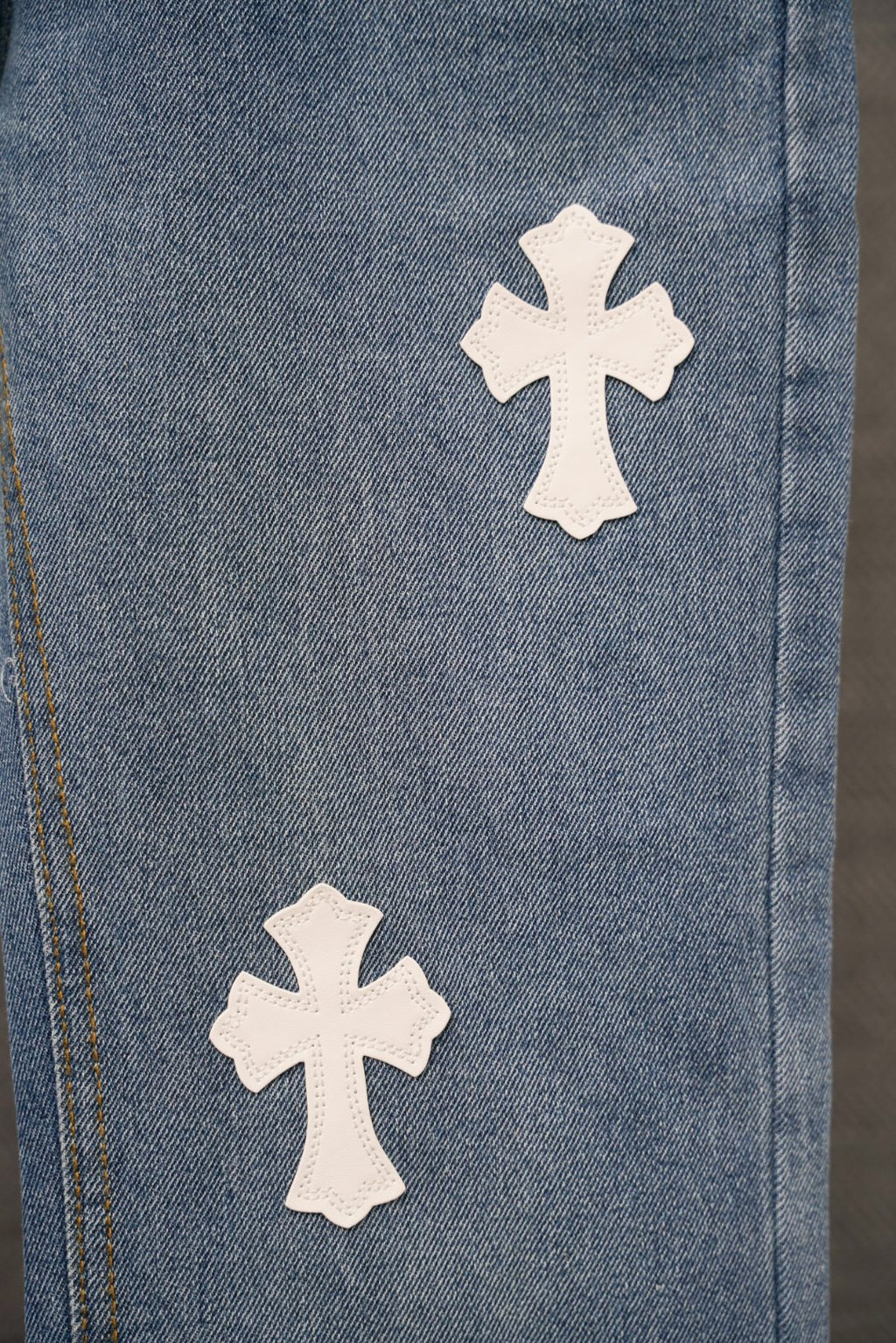 Blue denim pants with two white cross patches along the side seam.