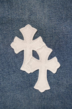 Denim pants with a large white cross patch stitched onto blue fabric.