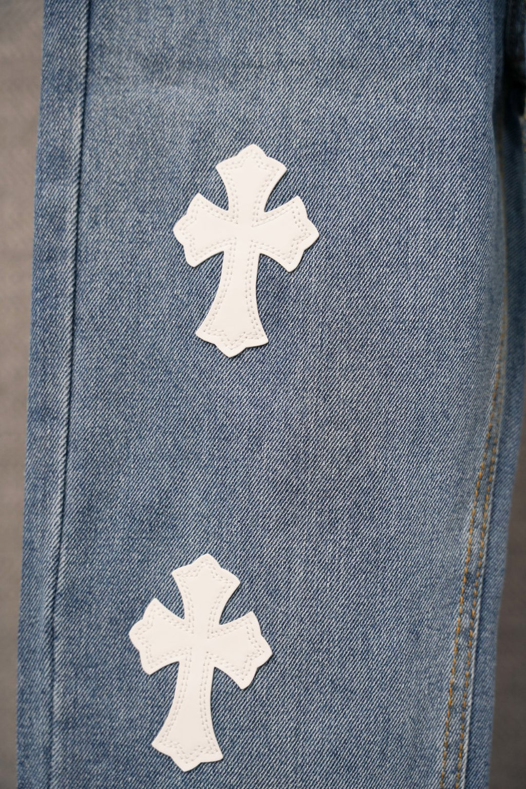 Blue denim pants with two white cross patches near the lower leg.