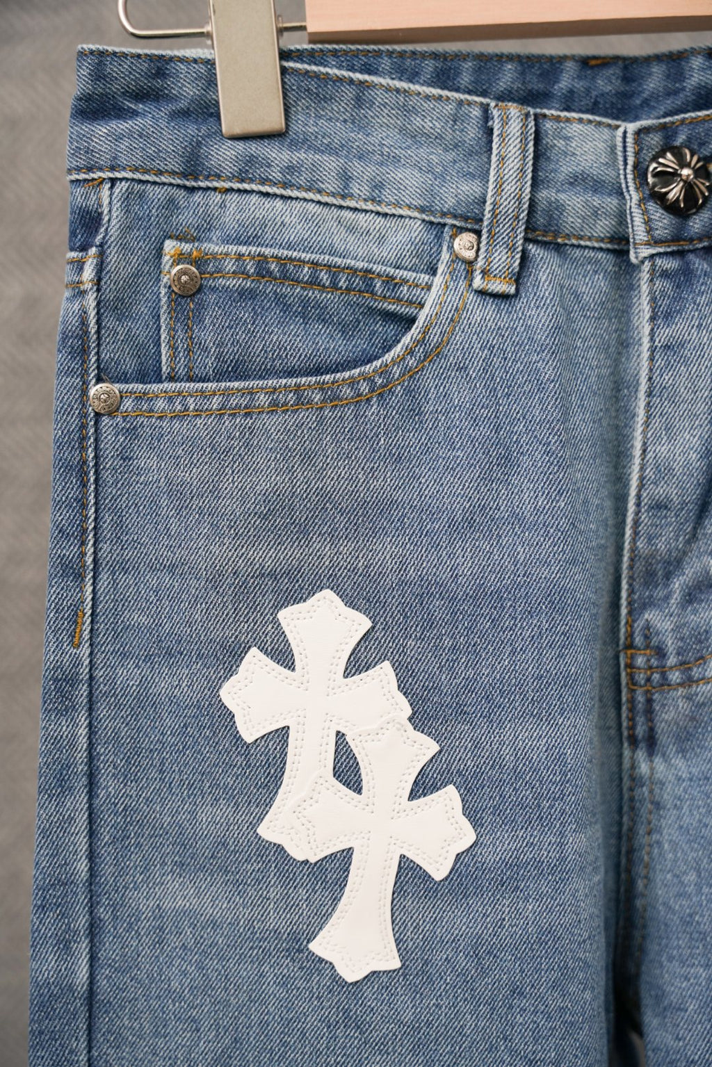 Blue denim pants front panel with coin pocket and large white cross patch.