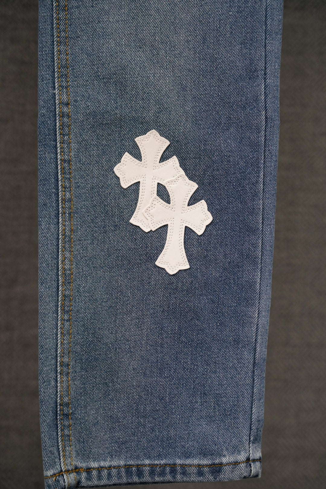 Blue denim pants leg with a single white cross patch near the hem.