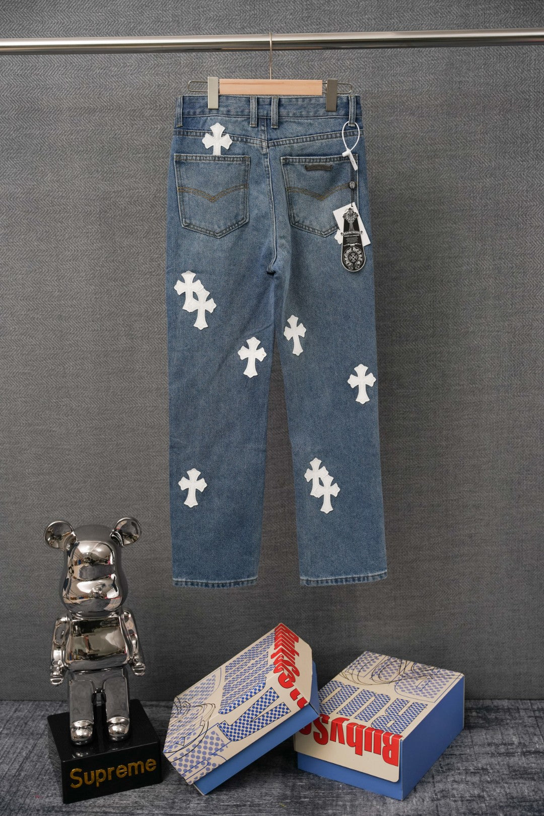 Blue denim pants with repeating white cross patches, relaxed straight fit.