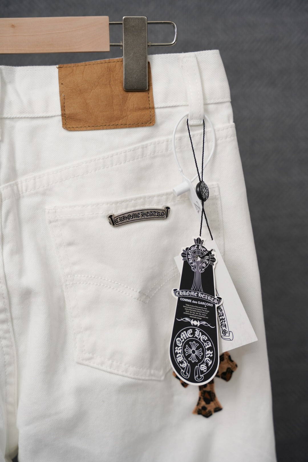 White denim pants with leather-look waistband patch and hanging charm tag