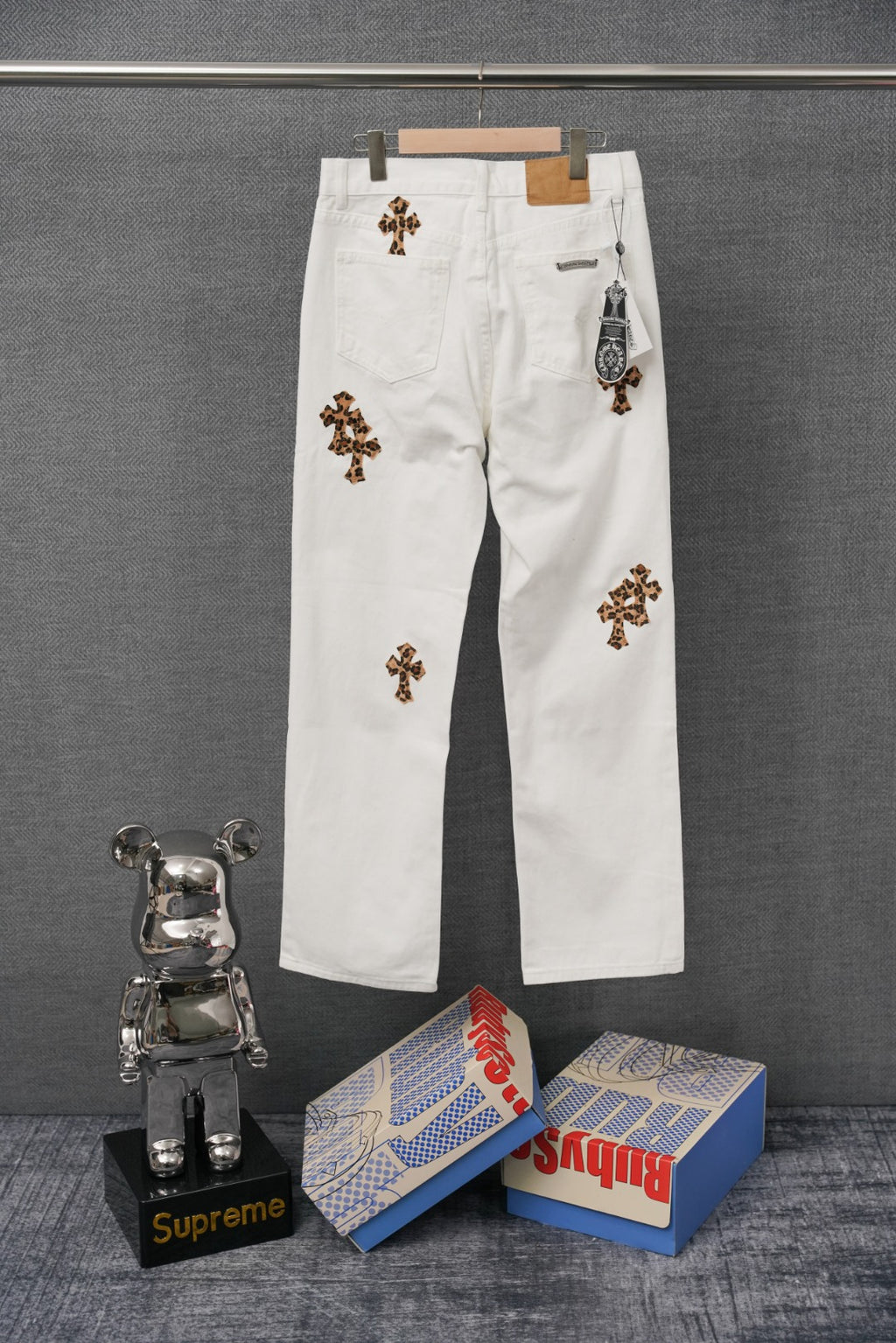White denim pants with leopard-print cross patches and small hanging tag at pocket