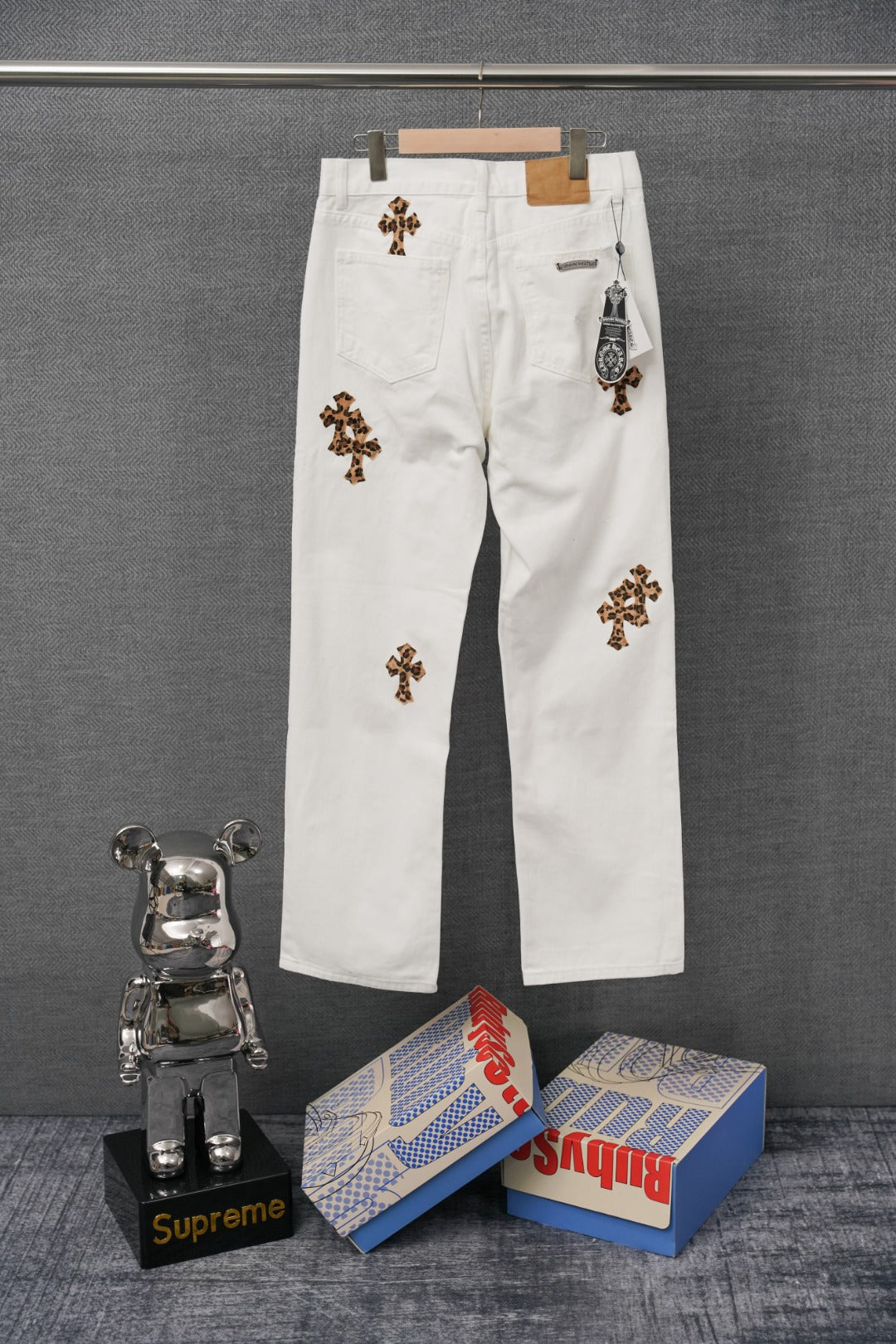 White denim pants with leopard-print cross patches and small hanging tag at pocket
