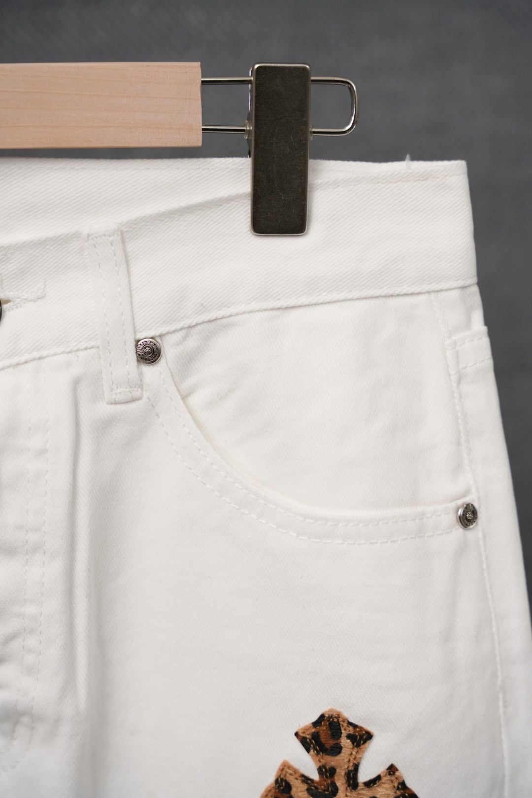 White pants with belt loops, front button, and printed patch at hem